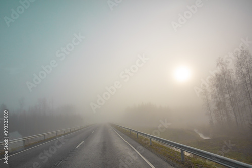 The sun is in the fog. Road and forest. Poor visibility. Autumn morning in November. Photo through the windshield of a car