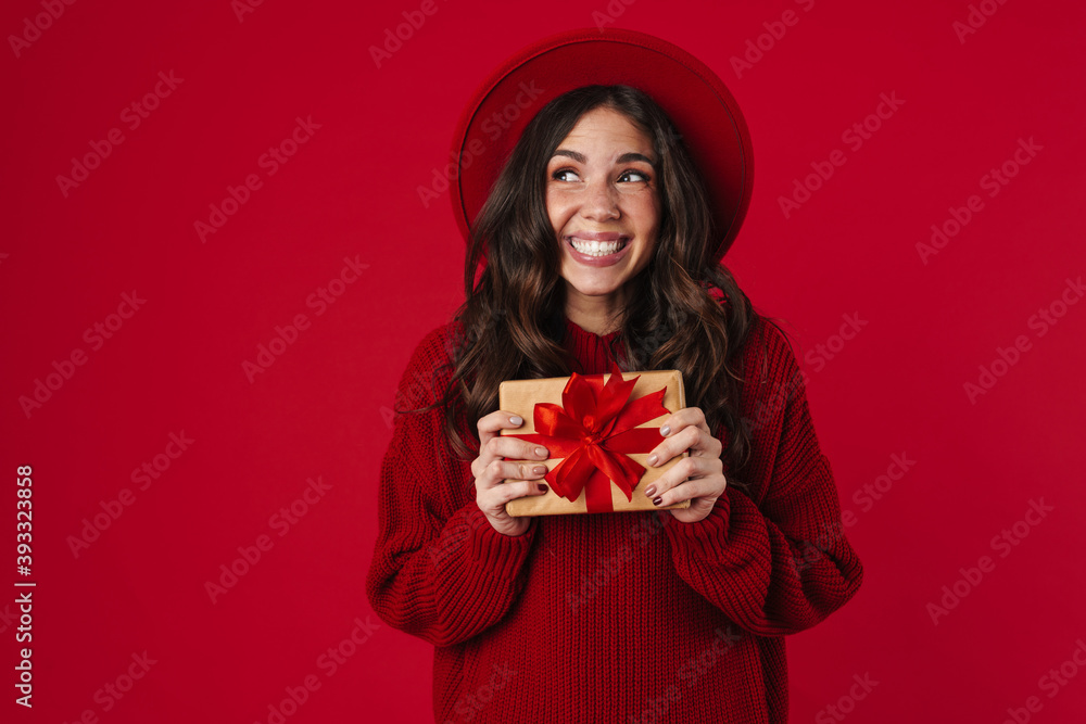 Joyful beautiful brunette girl in hat smiling and posing with gift box Joyful beautiful brunette girl in hat smiling and posing with gift box