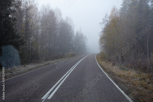 Poor visibility. The road is in heavy fog, along the edges of the road there is a forest. Autumn morning in November. Photo through the windshield of a car