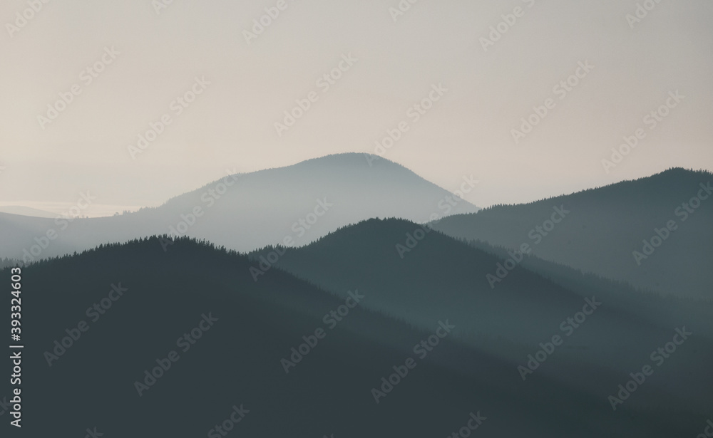 Beautiful, colorful mountain range landscape in soft blue tones with morning fog at sunrise.