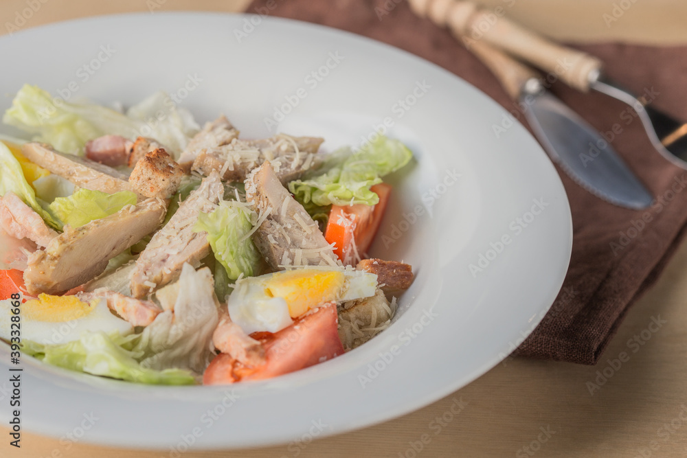 Lettuce and croutons topped with shredded cheese, Cezar salad on white plate over wooden table