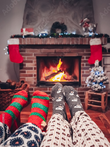 Feet in woollen socks by the Christmas fireplace. Couple relax by warm fire and warming up their feet in woollen socks. Close up on feet. Winter and Christmas holidays concept in a cabin.