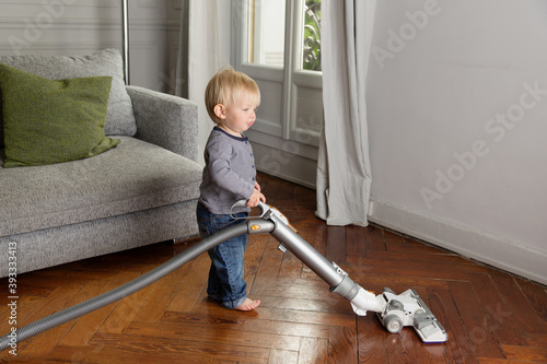 Cute baby using vacuum on hardwood floor in living room photo