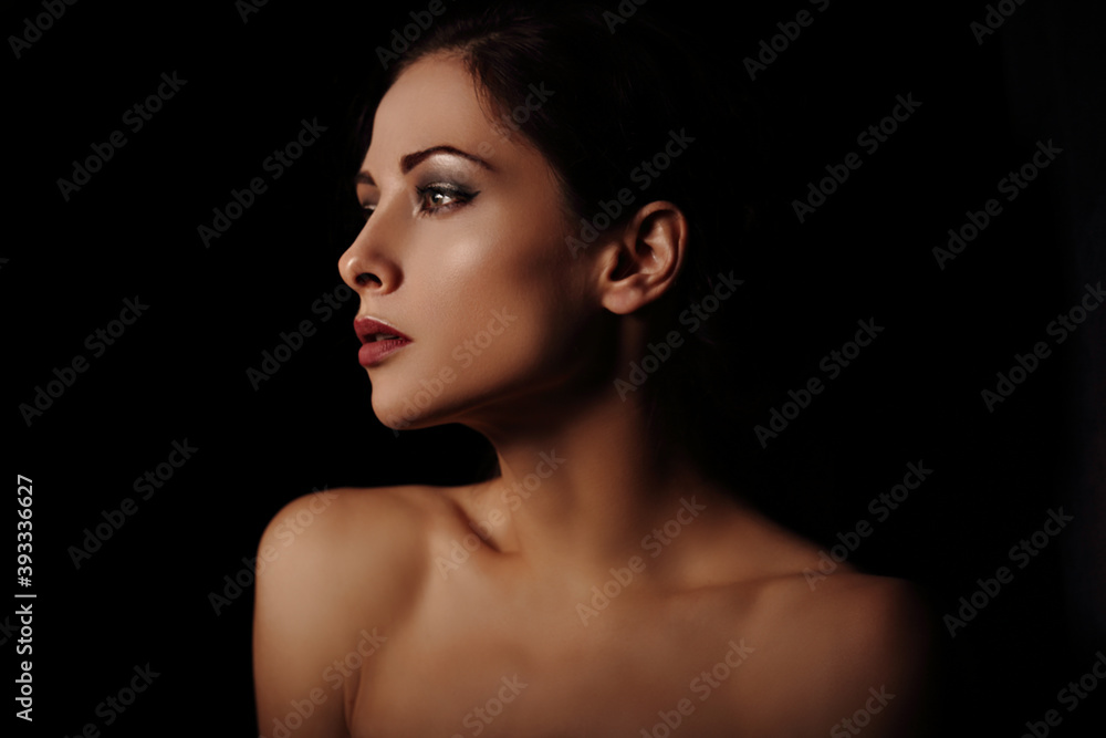 Beautiful mysterious woman in darkness with healthy neck, shoulders and golden health skin in shadows on dramatic black background with empty copy space. Closeup portrait. Art. Beautiful mysterious woman in darkness with healthy neck, shoulders and golden health skin in shadows on dramatic black background with empty copy space. Closeup portrait. Art.