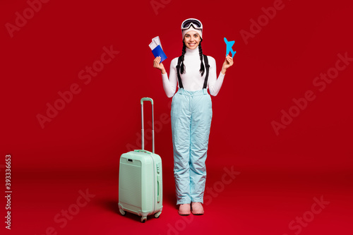 Fulll size photo of young happy girl with tails hold passport wear blue pants leaving for winter vacation isolated on red color background photo