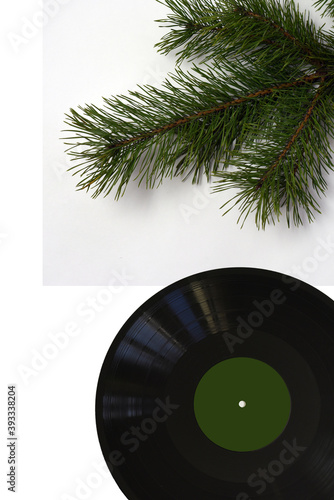 On a white vertical background  a live green pine branch and a black vinyl record in retro style.