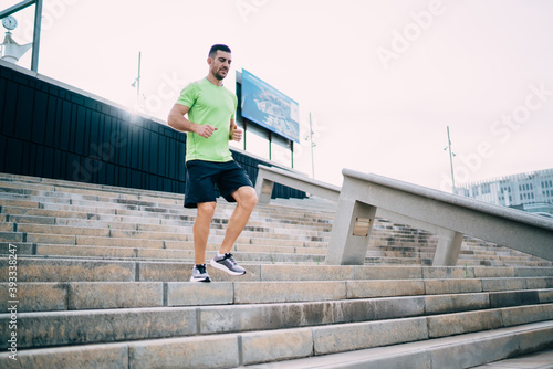 Muscular male runner in tracksuit enjoying active lifestyle on cardio workout feeling vitality and wellness, strong man jogger training endurance and muscular strength at stadium urban settings