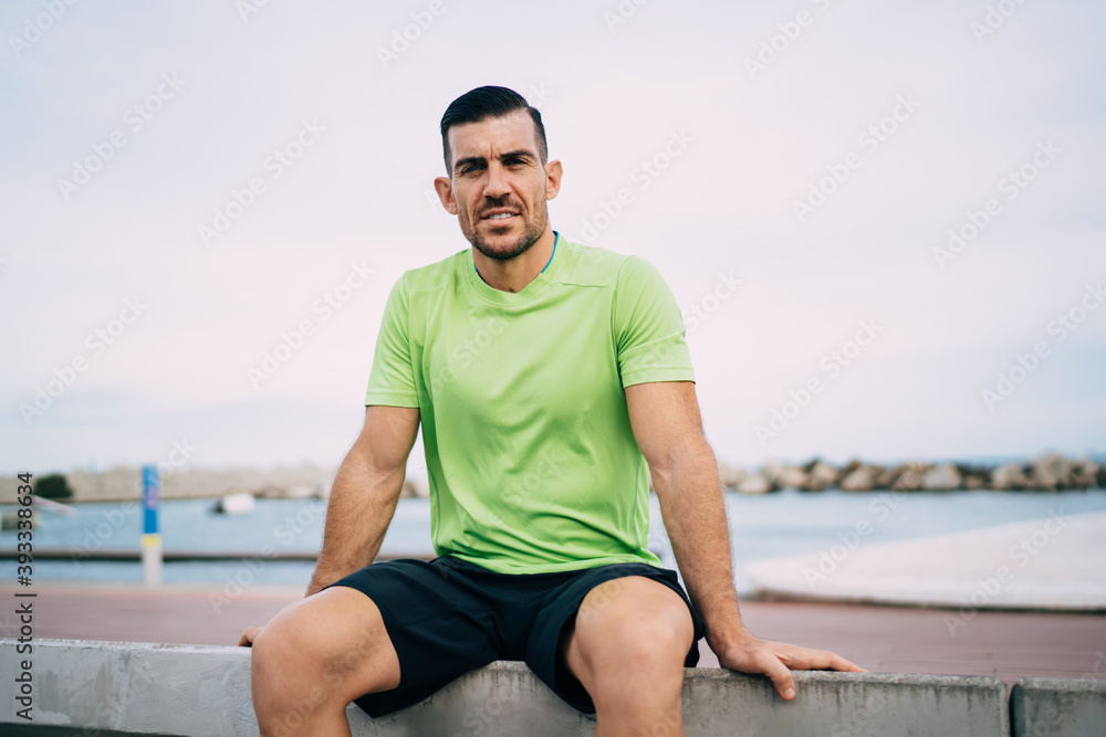 Portrait of muscular male jogger 30 years old looking at camera during workout break at embankment, strong sportsman dressed in active wear keeping healthy lifestyle and mental vitality wellness
