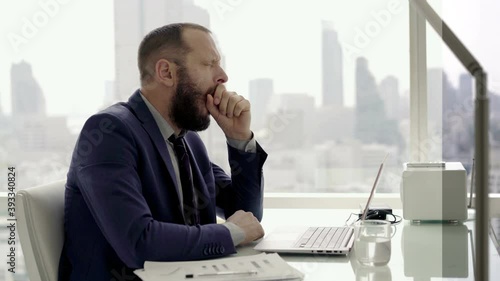 Tired businessman with laptop yawning in the office, 4K
