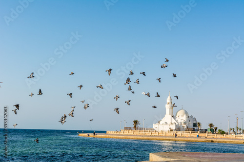 A group of doves flying over white mosque at the Jeddah Corniche coastal resort park near red sea in Jeddah, Kingdom of Saudi Arabia,