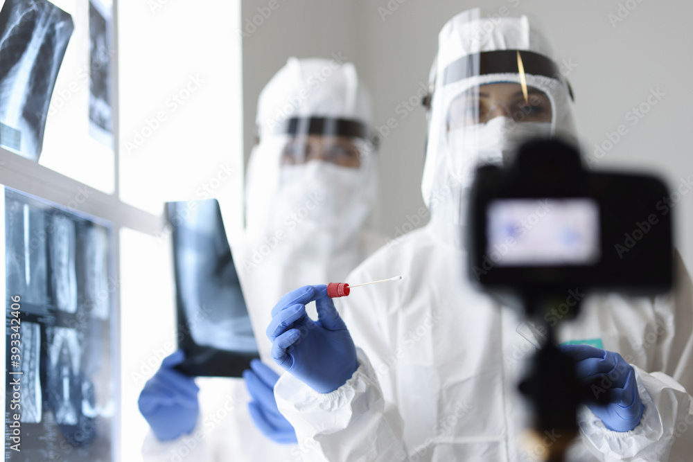 Two doctors in protective suits take an x-ray with test for analysis and shoot it on camera. Doctors work in coronavirus pandemic concept Two doctors in protective suits take an x-ray with test for analysis and shoot it on camera. Doctors work in coronavirus pandemic concept