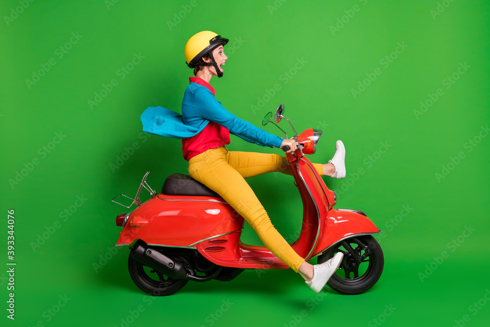 Full size profile side photo of young happy excited girl open mouth ride fast red moped isolated on green color background Full size profile side photo of young happy excited girl open mouth ride fast red moped isolated on green color background