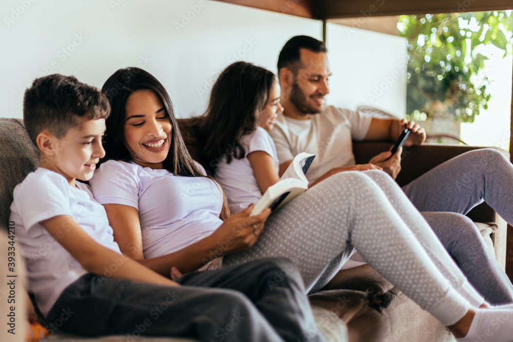Latin family enjoying the day together at home. Family reading together on the couch in the morning. Latin family enjoying the day together at home. Family reading together on the couch in the morning.