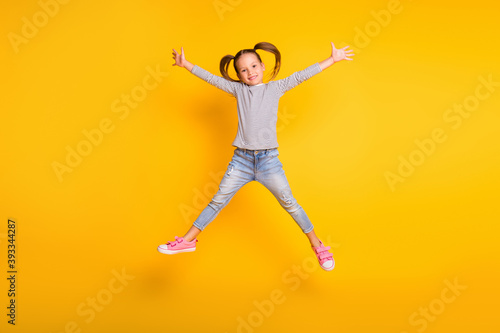 Full size photo of young happy positive little girl child kid jump raise hands up isolated on yellow color background