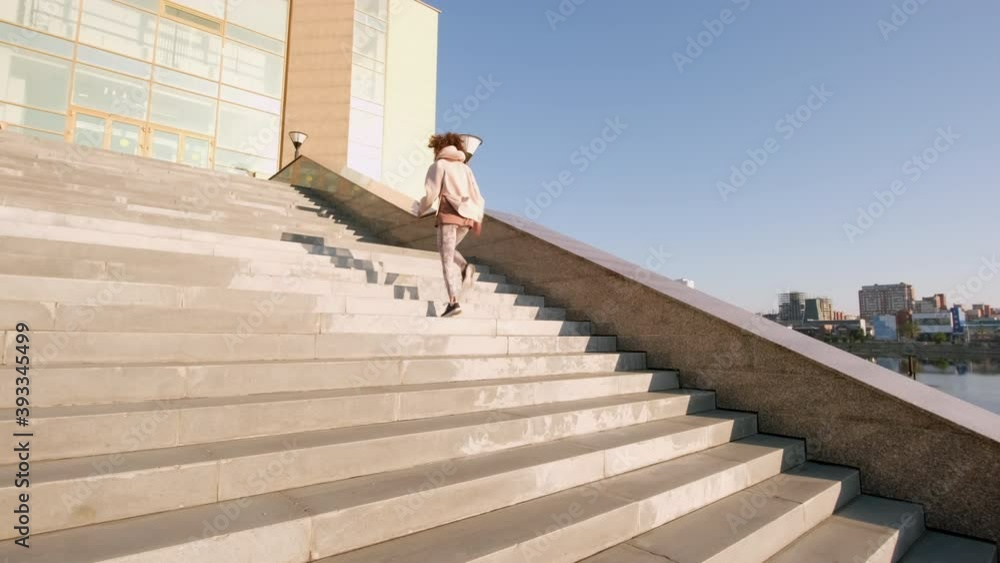 Slow-motion full back-view shot of slim female jogger doing morning cardio workout going up stairs in city centre in daylight Slow-motion full back-view shot of slim female jogger doing morning cardio workout going up stairs in city centre in daylight