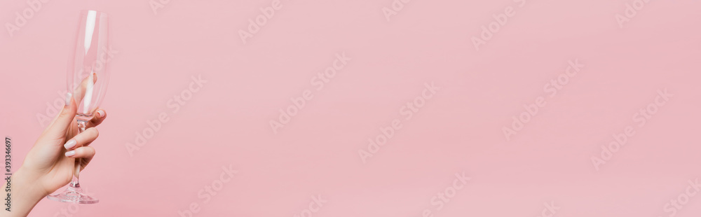 partial view of woman holding empty champagne glass isolated on pink, banner partial view of woman holding empty champagne glass isolated on pink, banner