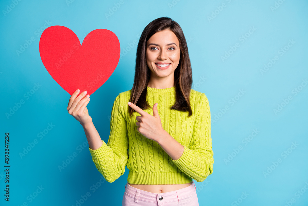 Photo portrait of woman holding big red heart in one hand pointing finger isolated on pastel blue colored background Photo portrait of woman holding big red heart in one hand pointing finger isolated on pastel blue colored background