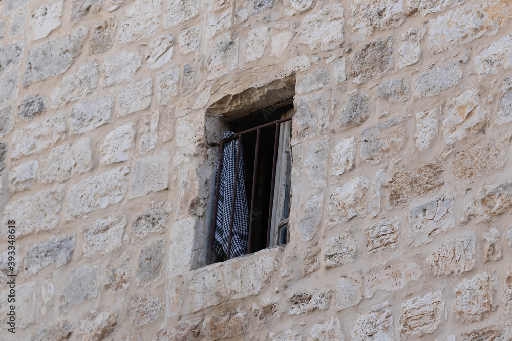 An arabic  headscarf with a national pattern hangs on a metal lattice in a building window on the Via Dolorosa Street in the old city of Jerusalem in Israel