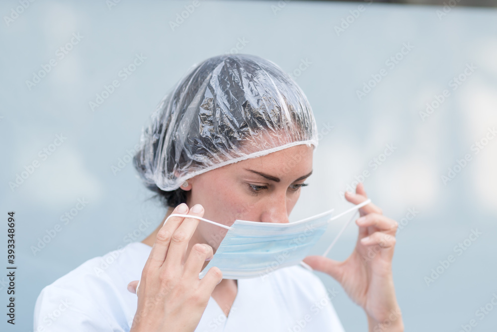 Portrait of a woman doctor putting on and fixing her surgical protective mask before her work shift