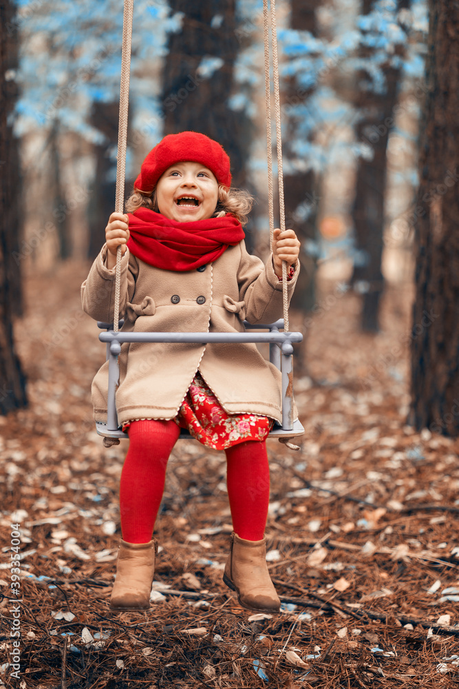 Little beautiful girl with toys walks in the autumn forest. Rides on a swing.