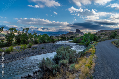Butte and river under dramatic clouds with distance mountains and trees and shrub in the foreground, Castle Rock, South Fork Shoshone River, Cody, Wyoming photo