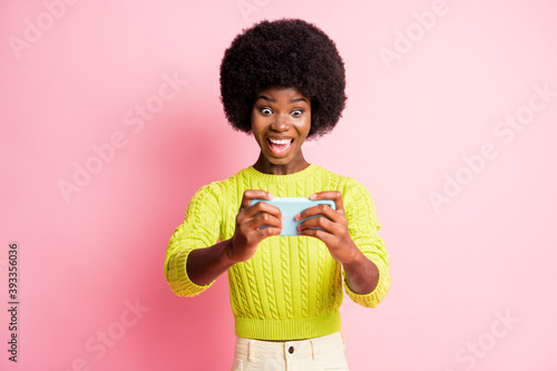 Photo portrait of excited screaming gamer girl holding phone in two hands isolated on pastel pink colored background