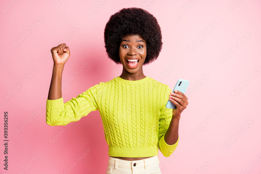 Photo portrait of excited celebrating woman holding phone in one hand isolated on pastel pink colored background