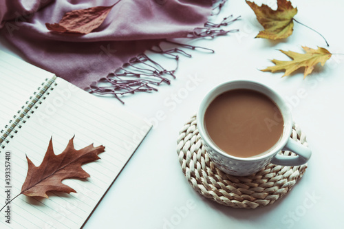 Autumn flat lay with coffee cup, notepad, fallen leaves and pink shawl on white background. Top view, copy space