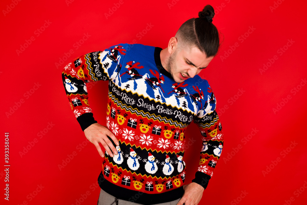 Young handsome Caucasian man wearing Christmas sweater against red wall, Suffering of backache, touching back with hand, muscular pain