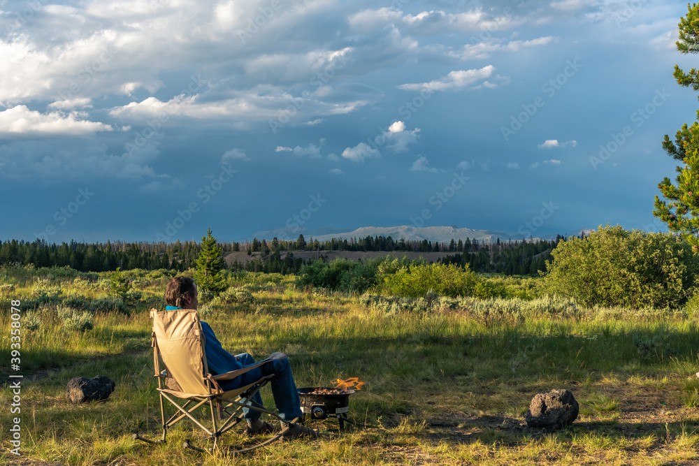 A man sitting on a rocking chair enjoying a campfire and the view