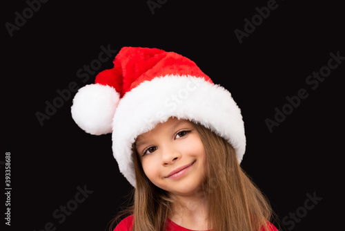 A little beautiful girl in a red Christmas hat poses.