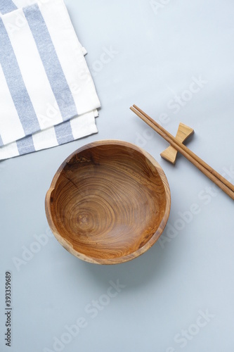Mangkok kayu or empty wooden bowl and chopsticks on blue stripes napkin. Isolated soft gray background, top view