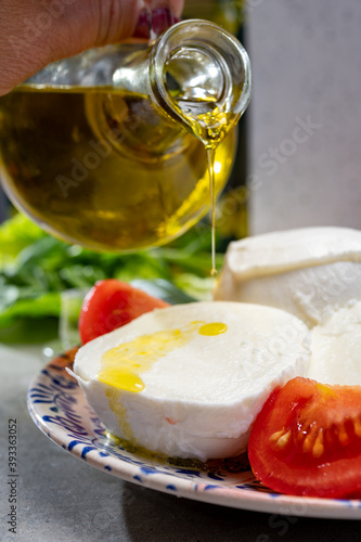Making of fresh caprese salad with soft Italian cheese from Campania buffalo mozzarella with tomatoes, basil and olive oil