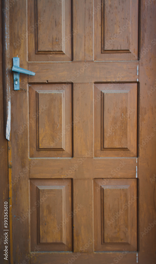A brown wooden door with ribs and metallic handle closeup A brown wooden door with ribs and metallic handle closeup