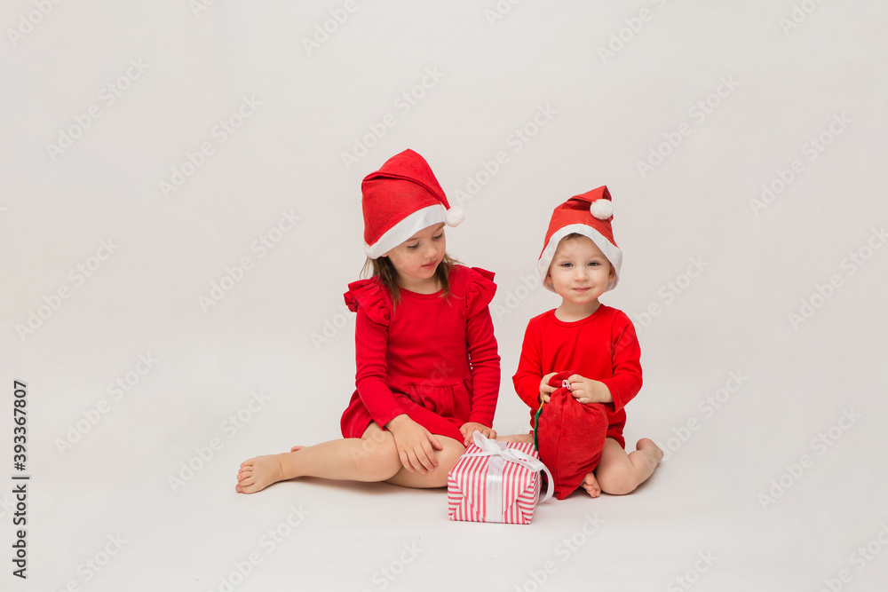 Obraz premium little girl and boy in Christmas hats with gifts on a white background