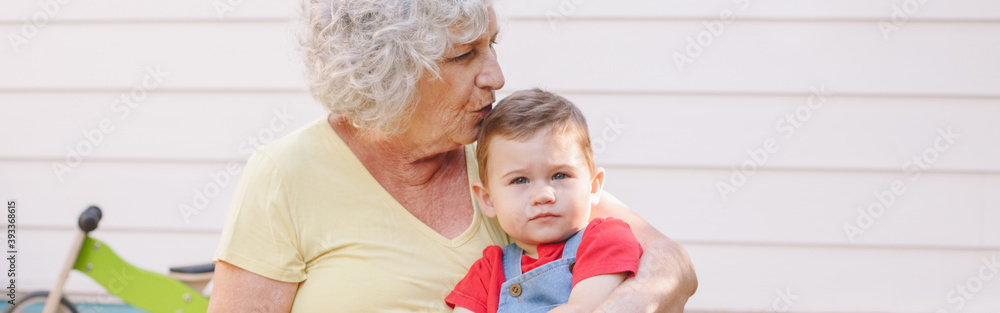 Grandmother kissing grandson boy. Bonding of relatives and generation communication. Old woman with baby spending time together outdoors. Web banner header. Grandmother kissing grandson boy. Bonding of relatives and generation communication. Old woman with baby spending time together outdoors. Web banner header.