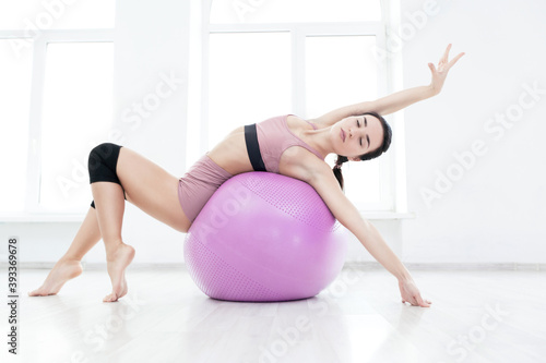 Young slender girl strengthens the back muscles with the help of fitness ball