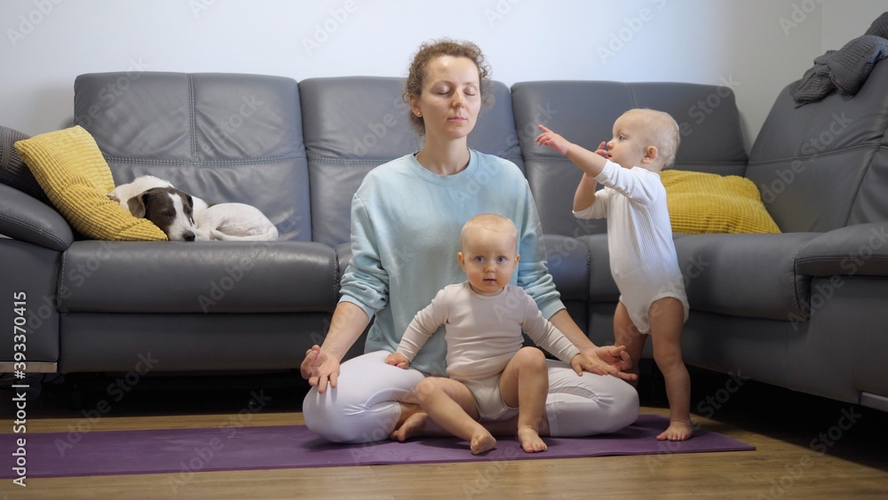 Self care and personal time of busy parents life. Single mom tries to meditate on yoga mat at home with two active kids around distracting her Self care and personal time of busy parents life. Single mom tries to meditate on yoga mat at home with two active kids around distracting her