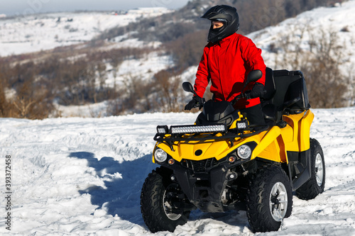 Young man driver on the ATV quad bike stand in heavy snow with deep wheel track. Moto winter sports.