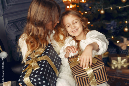 Beautiful mother in a white dress. Family with cristmas gifts. Girls near fireplace.