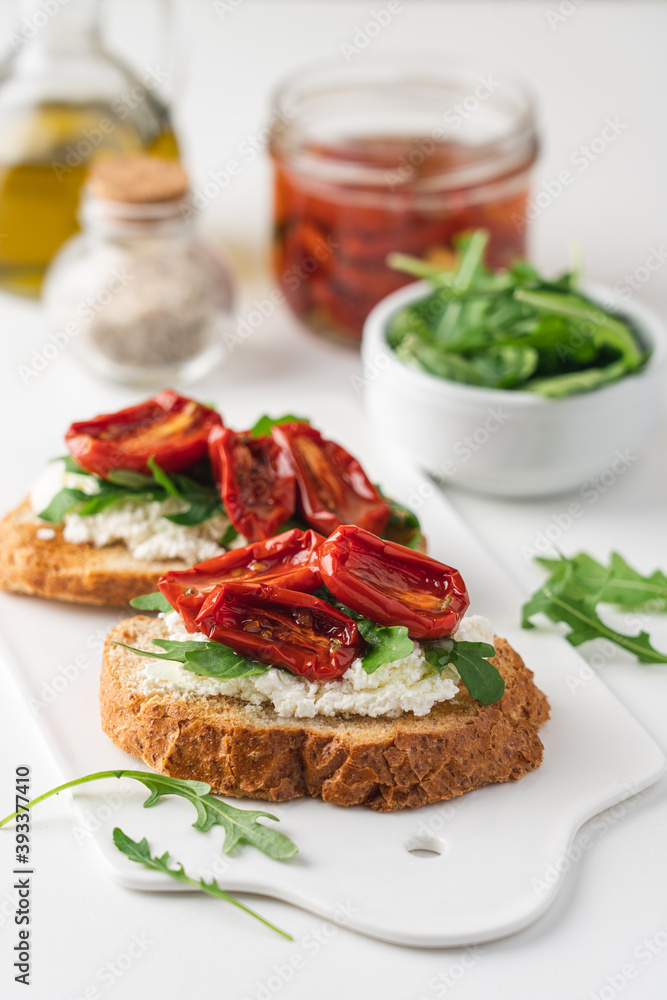 Bruschetta with sunny dried tomatoes and arugula. Delicious breakfast or wine snack. White background, close-up, top view