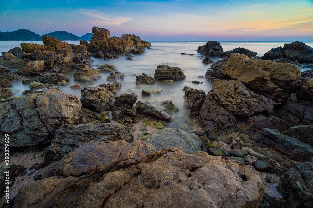 Beautiful rocks by the beach, splashed by the sea. With the sky and the sunset view on the landscape background long exposure shots.