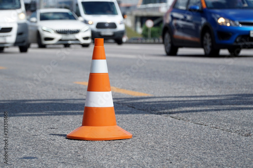 Road cone stands on the road against the backdrop of fast-moving cars.