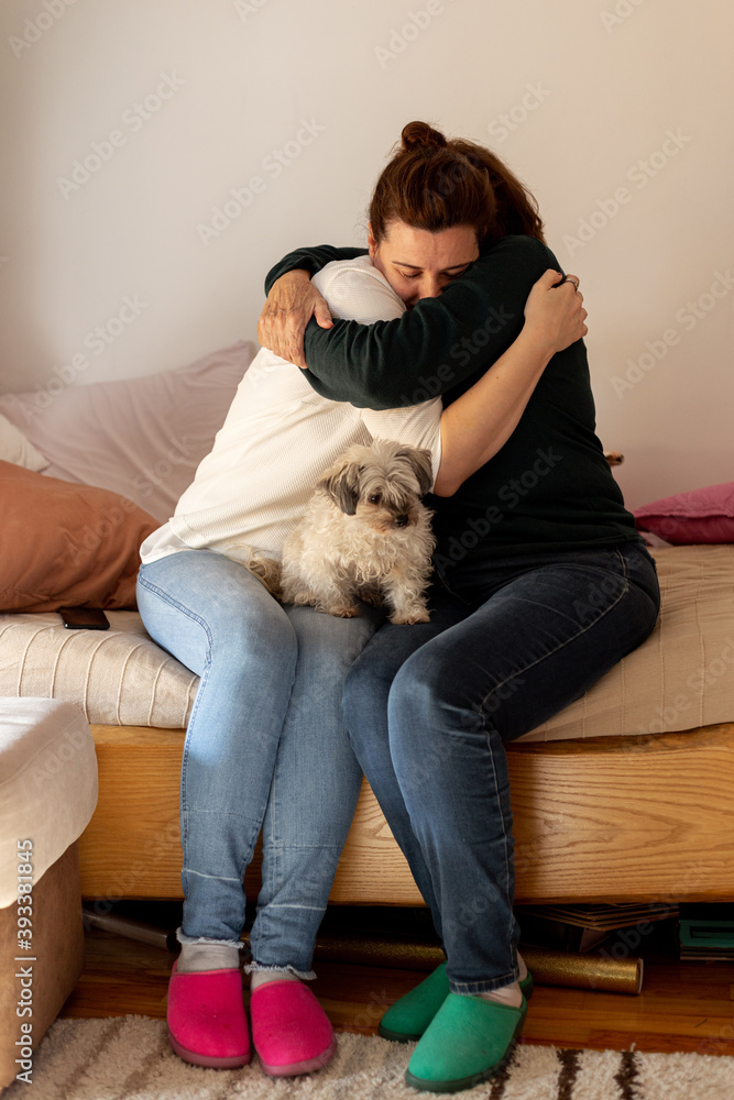 Elderly mother embrace and hug adult daughter with little dog sitting in their lap. Genuine moment of family love. Elderly mother embrace and hug adult daughter with little dog sitting in their lap. Genuine moment of family love.