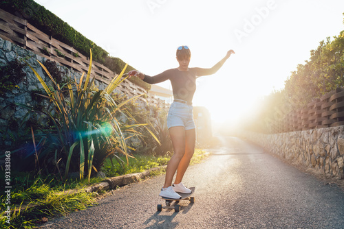 Young slim casually dressed woman skater enjoying spending free time on hobby in sunny evening, beautiful caucasian female 20s practicing on board enjoying active lifestyle and weekends on rural area #393383863