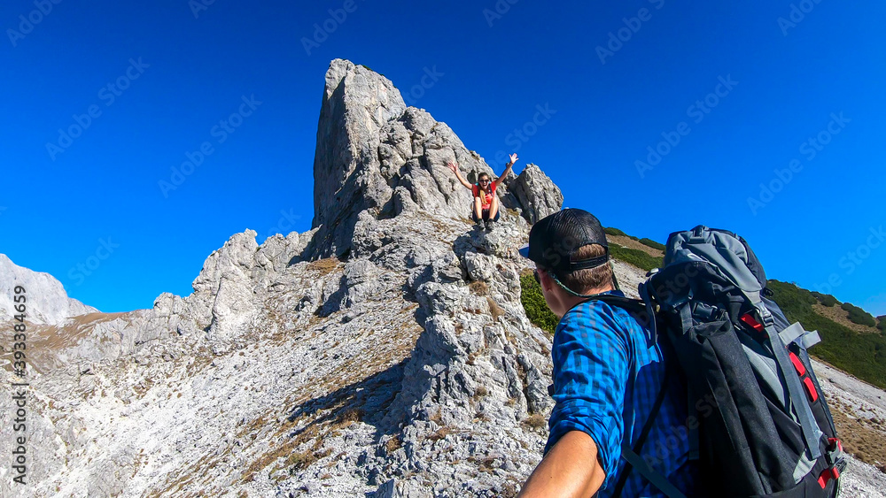 A couple hiking in Hochschwab region in Austrian Alps. They are climbing a sharp rock. The man is taking a selfie. Idyllic landscape. Freedom and wilderness. Pathless wandering. Massive mountain chain
