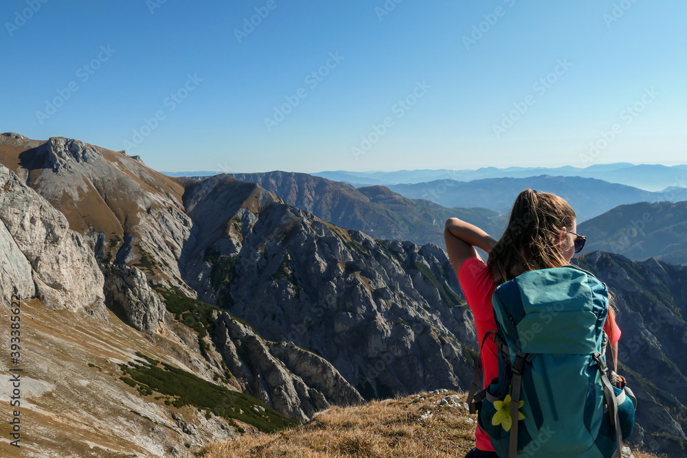A woman with big blue backpack enjoying the view on valley from top of a mountain in Hochschwab region in Austrian Alps. The flora overgrowing the slopes is turning golden. Freedom. She is happy