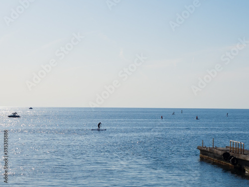 Calm blue sea with boats and surfers in it under clear skies