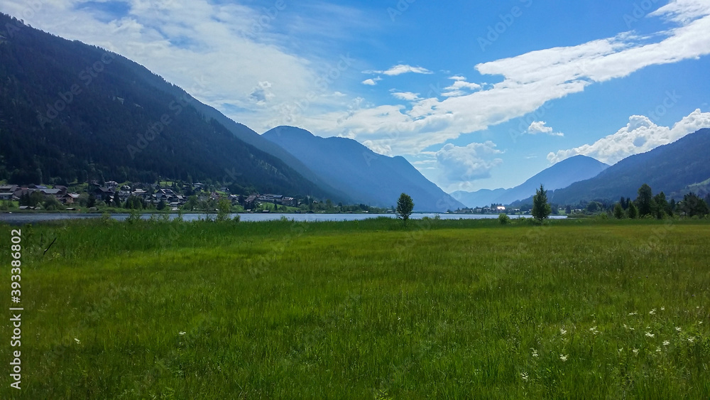 An idyllic view on the blossoming meadow and distant Weissensee lake surrounded by the Austrian Alps. Joyfulness and happiness. Many mountain chains in the back. Sunny day
