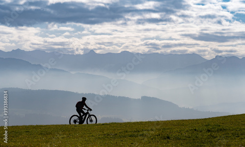 Woman as silhouette riding her electric mountain bike in the Allgaeu alps near Oberstaufen with awesome view into the Bregenz Wald Mountains, Vorarlberg , Austria